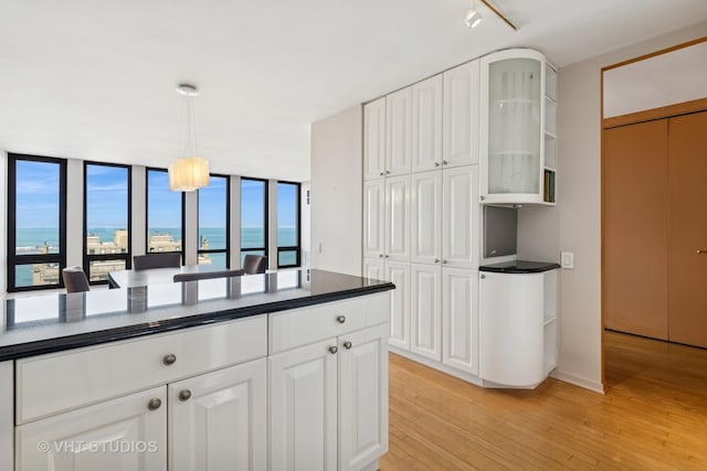 kitchen with light wood-type flooring, dark countertops, white cabinets, glass insert cabinets, and hanging light fixtures