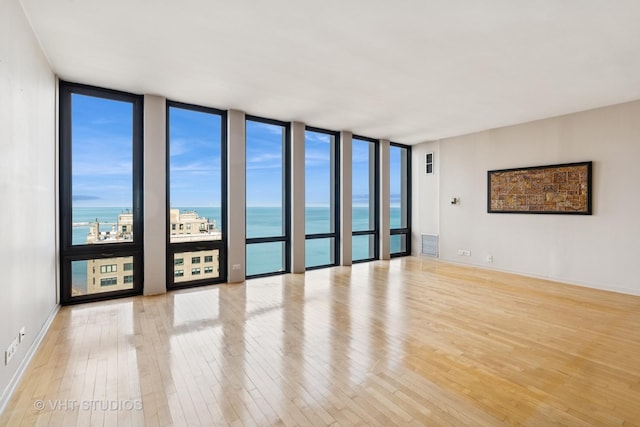 spare room with baseboards, a water view, wood finished floors, and floor to ceiling windows