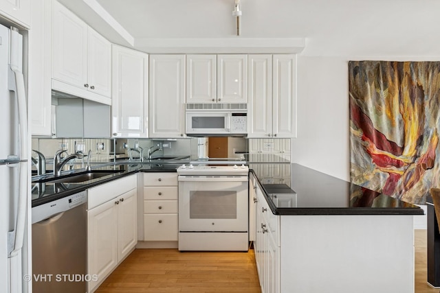 kitchen featuring dark countertops, white appliances, a peninsula, and a sink