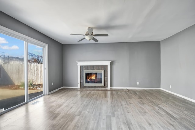 unfurnished living room featuring hardwood / wood-style flooring, ceiling fan, and a tiled fireplace