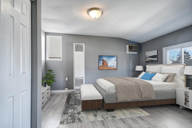 bedroom with a wall mounted air conditioner, lofted ceiling, and light hardwood / wood-style flooring