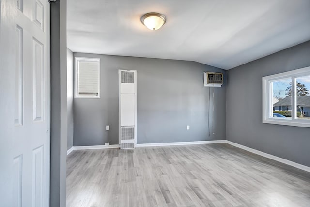 empty room with lofted ceiling, a wall mounted air conditioner, and light wood-type flooring