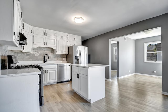 kitchen with a kitchen island, tasteful backsplash, appliances with stainless steel finishes, white cabinets, and light wood-type flooring