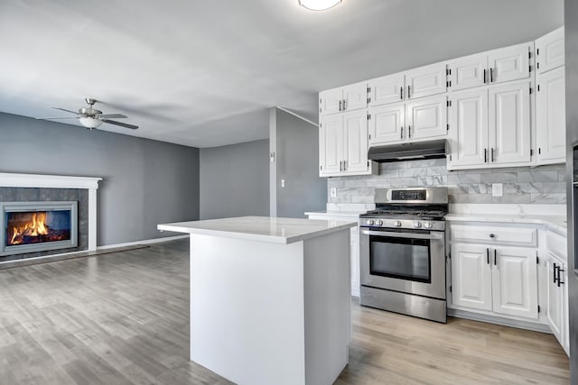 kitchen with stainless steel gas range oven, a center island, white cabinets, and a tiled fireplace