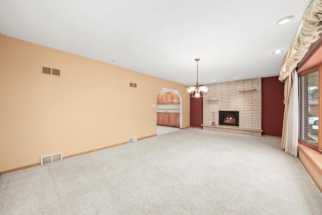 unfurnished living room featuring a fireplace, light carpet, and a chandelier