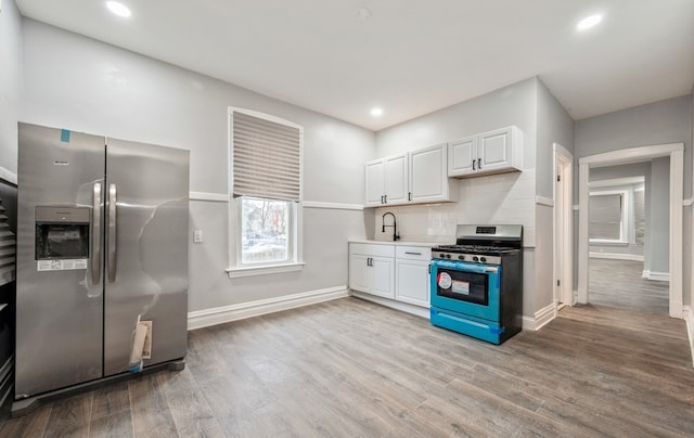 kitchen with white cabinetry, sink, stainless steel appliances, backsplash, and light wood-type flooring