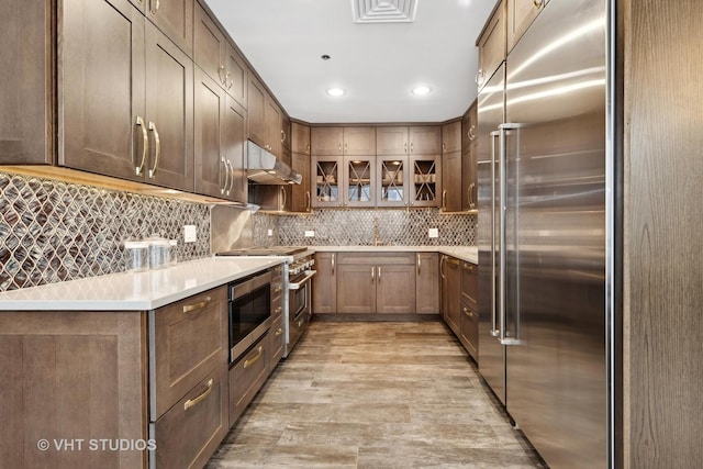 kitchen with built in appliances, decorative backsplash, light hardwood / wood-style flooring, and sink