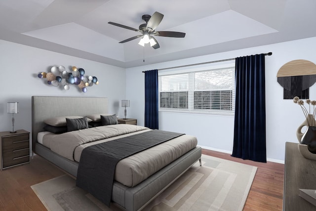 bedroom featuring dark hardwood / wood-style flooring, a tray ceiling, and ceiling fan