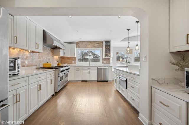 kitchen featuring white cabinets, wall chimney exhaust hood, light stone counters, and stainless steel appliances