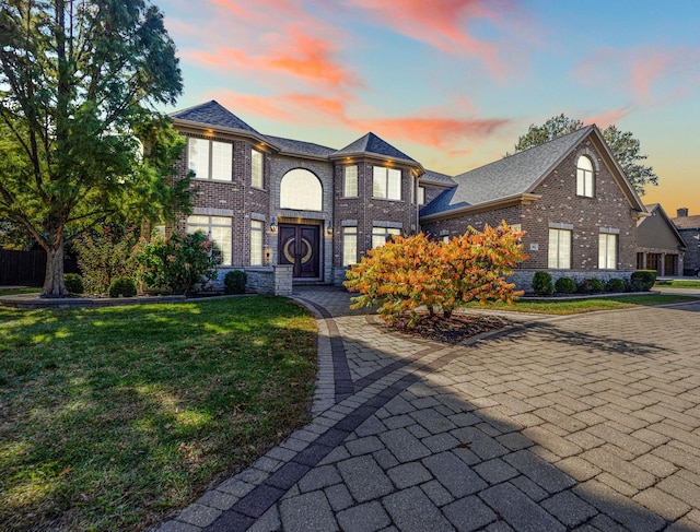 traditional-style house featuring roof with shingles, a front lawn, and brick siding