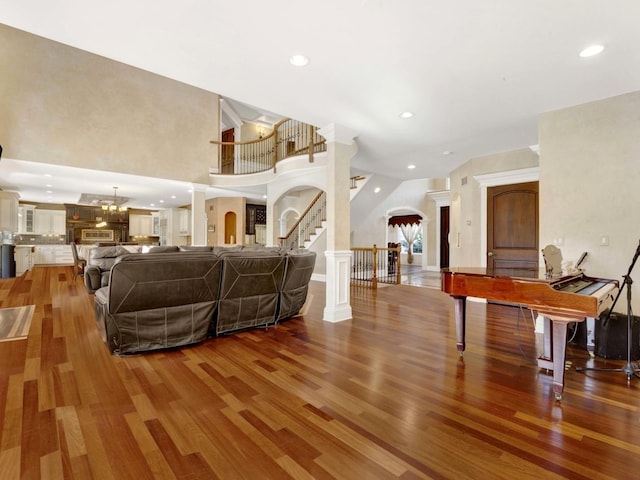 living room with decorative columns, arched walkways, wood finished floors, stairs, and recessed lighting