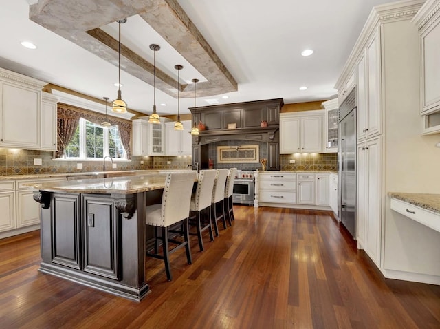 kitchen with a breakfast bar area, dark wood-type flooring, high quality appliances, a tray ceiling, and glass insert cabinets