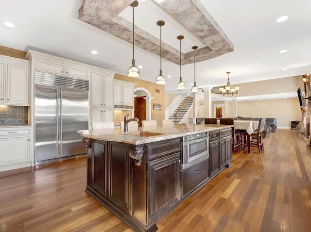 kitchen featuring a raised ceiling, dark wood-type flooring, stainless steel built in fridge, a sink, and dark brown cabinets