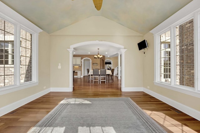 interior space with arched walkways, wood finished floors, vaulted ceiling, decorative columns, and an inviting chandelier