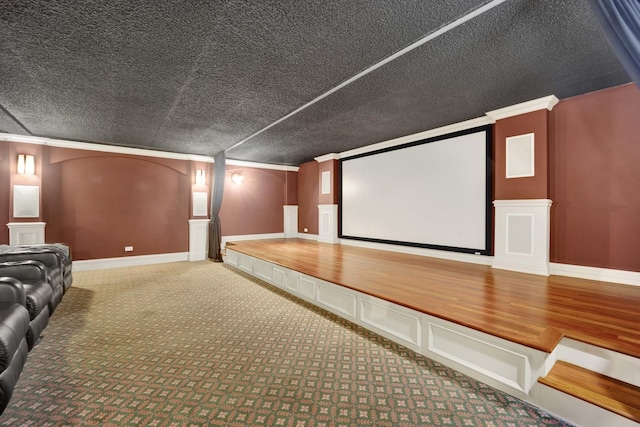 carpeted home theater room with a textured ceiling, ornamental molding, baseboards, and a decorative wall