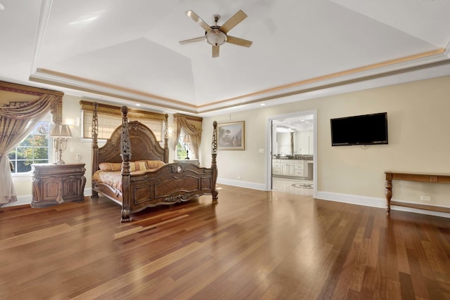 bedroom featuring a tray ceiling, baseboards, ensuite bathroom, and wood finished floors