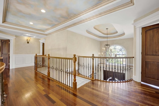 hallway featuring a tray ceiling, wood finished floors, a decorative wall, and an inviting chandelier