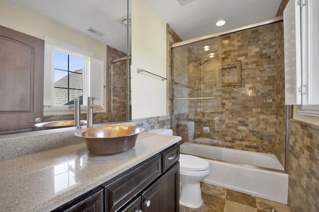 bathroom with visible vents, toilet, enclosed tub / shower combo, vanity, and tile walls