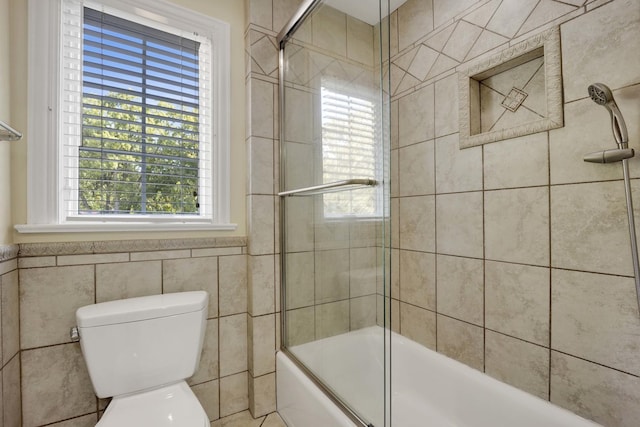 full bath with toilet, shower / bath combination with glass door, and tile walls