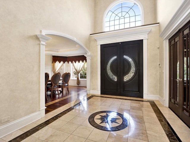 foyer with a towering ceiling, decorative columns, baseboards, and crown molding