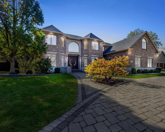 view of front of house with a front yard, brick siding, and roof with shingles