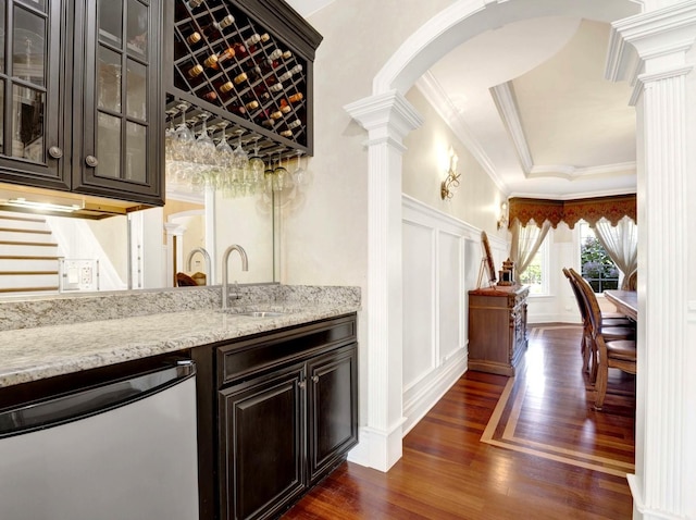 bar with decorative columns, dishwashing machine, dark wood-style floors, crown molding, and a decorative wall