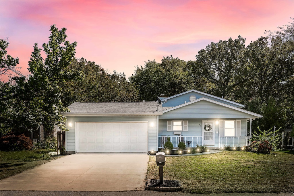 single story home featuring covered porch, a garage, and a yard