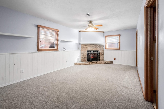 unfurnished living room with carpet floors, a brick fireplace, plenty of natural light, and ceiling fan