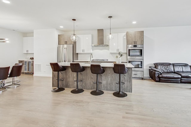 kitchen with stainless steel appliances, wall chimney range hood, decorative light fixtures, white cabinets, and a breakfast bar area