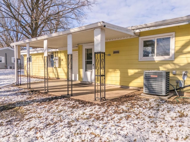 snow covered rear of property featuring central AC