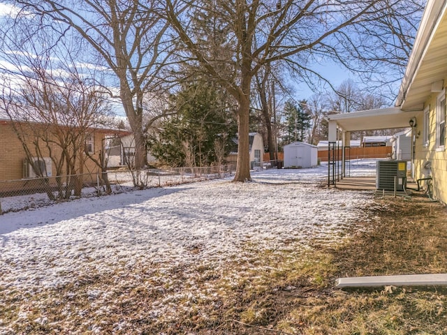 yard layered in snow with central air condition unit and a storage shed