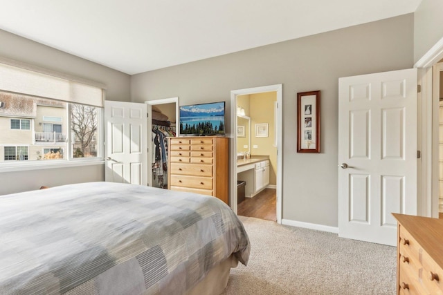 bedroom with ensuite bath, a walk in closet, light carpet, and a closet