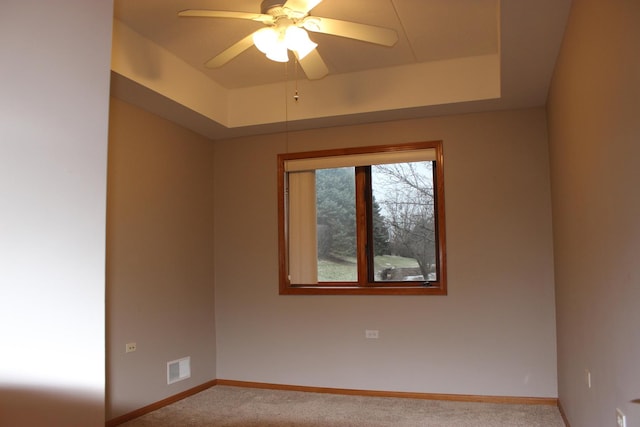 unfurnished room featuring ceiling fan, light colored carpet, and a tray ceiling