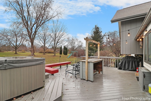 deck featuring a playground, a yard, and a hot tub