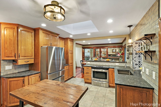 kitchen featuring a skylight, sink, hanging light fixtures, kitchen peninsula, and appliances with stainless steel finishes