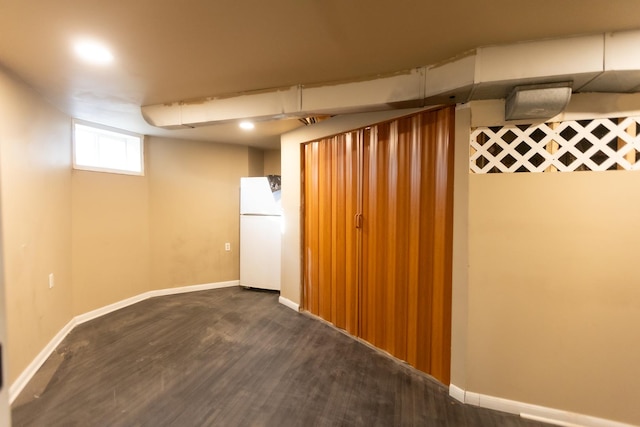 basement with baseboards, wood finished floors, and freestanding refrigerator