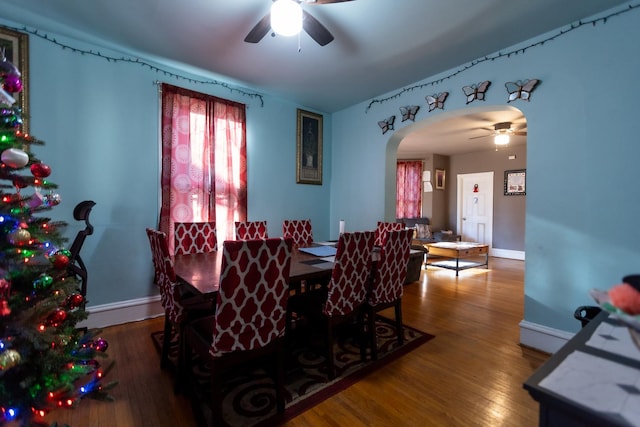 dining space featuring arched walkways, ceiling fan, baseboards, and wood finished floors