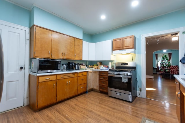 kitchen with arched walkways, stainless steel appliances, light countertops, brown cabinetry, and under cabinet range hood