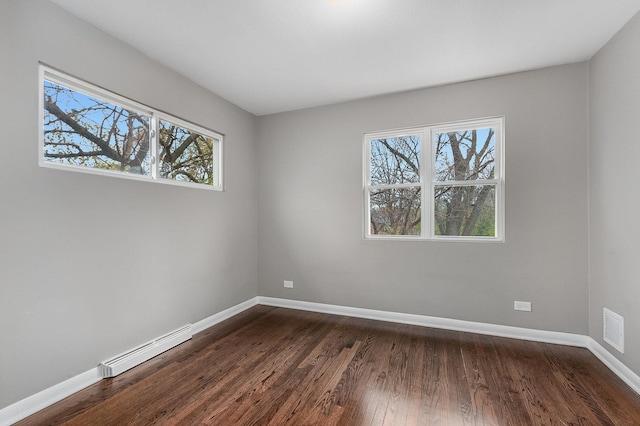 spare room featuring dark hardwood / wood-style flooring, a wealth of natural light, and a baseboard heating unit