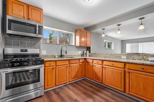 kitchen with dark wood-type flooring, sink, light stone countertops, decorative light fixtures, and stainless steel appliances