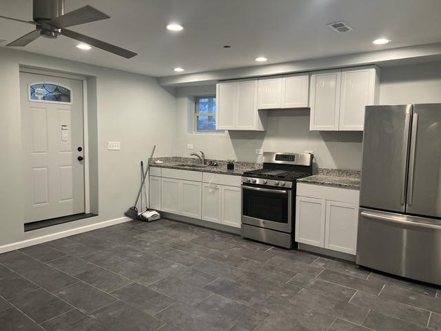 kitchen with white cabinetry, dark stone counters, appliances with stainless steel finishes, ceiling fan, and sink