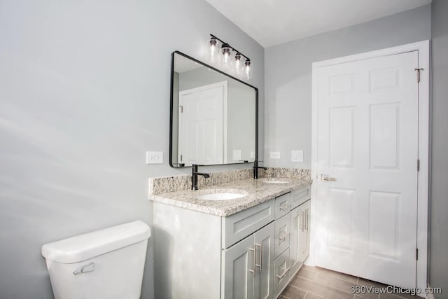 full bathroom with toilet, double vanity, a sink, and wood finish floors