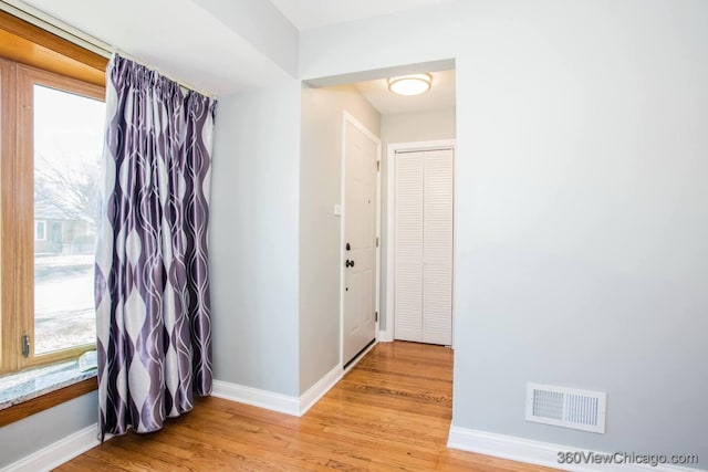 corridor featuring light wood-style flooring, visible vents, and baseboards