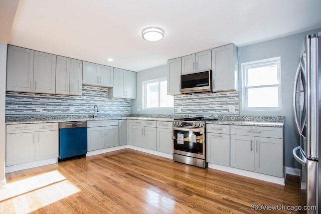 kitchen with light hardwood / wood-style floors, light stone countertops, stainless steel appliances, and tasteful backsplash