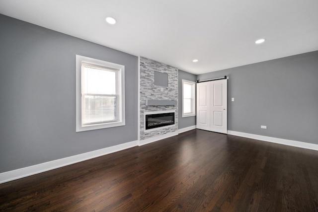 unfurnished living room featuring a barn door, dark hardwood / wood-style flooring, and a fireplace