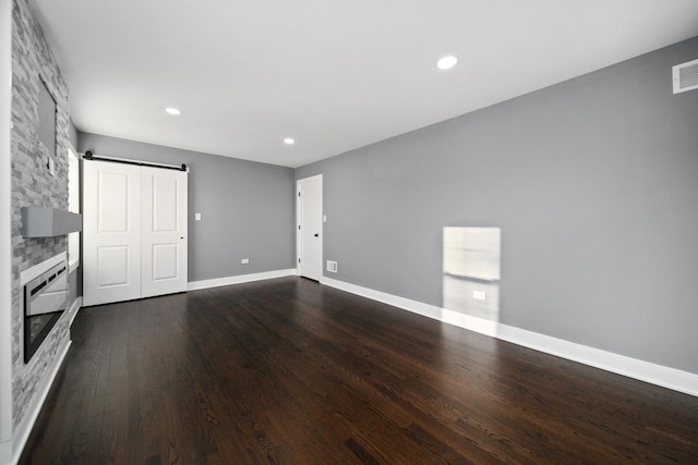 unfurnished living room with a fireplace, a barn door, and dark wood-type flooring