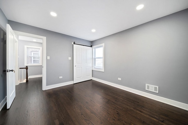 unfurnished bedroom featuring a barn door and dark hardwood / wood-style floors