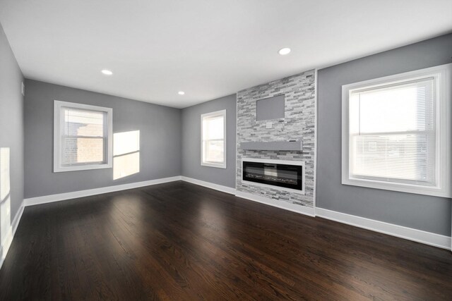 unfurnished living room with a stone fireplace and dark wood-type flooring