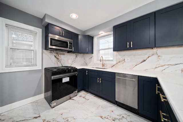 kitchen with light stone countertops, appliances with stainless steel finishes, backsplash, sink, and blue cabinetry