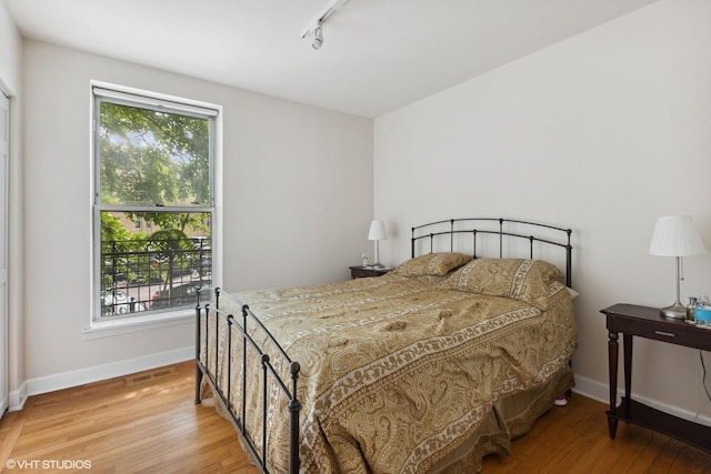 bedroom with hardwood / wood-style floors, track lighting, and multiple windows